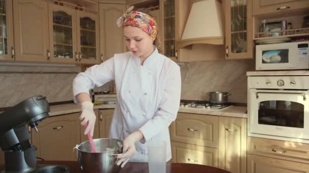 Женщина на кухне с рукой с силиконовым венчиком смешивает белый крем в стальной миске, чтобы сделать вкусный десерт — стоковое видео