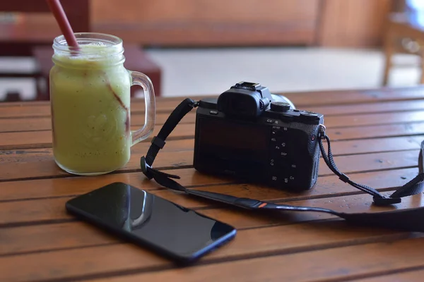 2020 索尼A7相机和诺基亚智能手机在一张装有果汁的木制桌子上 这张照片可以作为旅行背景 — 图库照片