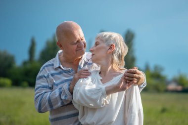 Mutlu yaşlı çift buluşuyor, sarılıyor ve gün batımında öpüşüyor.