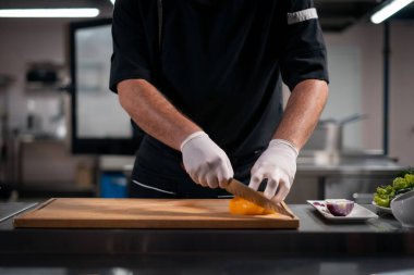 Aşçıya yakın eldiven giymiş eller mutfakta sarı biber kesiyor ya da doğruyor.