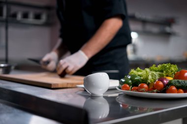 Tıbbi eldivenler giymiş aşçı şefi mutfakta Yunan salatası ya da sebze doğrayabilir. 
