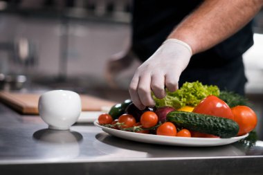 Şef aşçı elleri tıbbi eldivenlerle mutfakta sebzeli Yunan salatası hazırla.