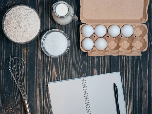 Boş yemek tarifi kitabı ve un, örümcekler, süt, şeker ahşap arka planda.