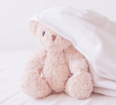 Beyaz battaniye içinde sevimli oyuncak bebek, oyuncak ayı en iyi arkadaşıyla saklambaç oynuyor. Sabahları iyi eğlenceler.