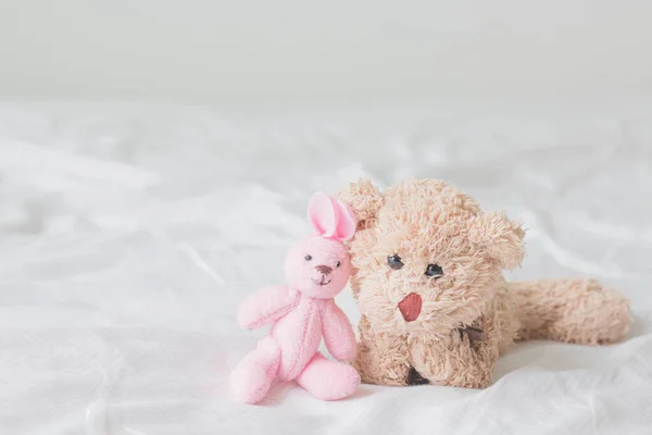 Oyuncak ayı ve pembe tavşan yatakta yatıyor..
