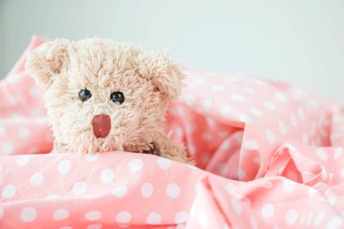 Küçük sevimli bir oyuncak ayı pembe bir battaniyenin üzerinde uyuyor, Doll dinleniyor.