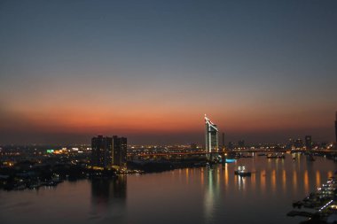 Aydınlatılmış şehir binaları ve günbatımı gökyüzü liman suyuna yansıyor