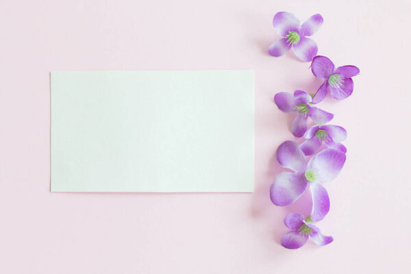 small white paper sheet and plastic purple flowers on pink background