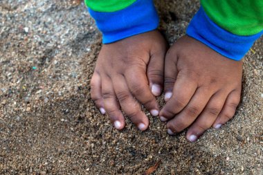 Çocuğun elleri kumla oynuyor.