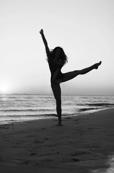 Девушка занимается гимнастикой на пляже на закате — стоковое фото
