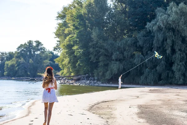 一个运行在春天，夏天，在沙滩上风筝的家伙的女孩. — 图库照片