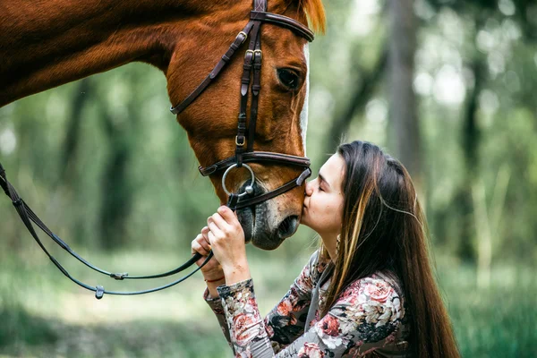 Chica joven con el pelo largo besando a un caballo — Foto de Stock