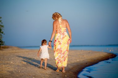 Kumsalda yürüyen küçük bir çocuk ile anne