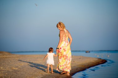 Kumsalda yürüyen küçük bir çocuk ile anne