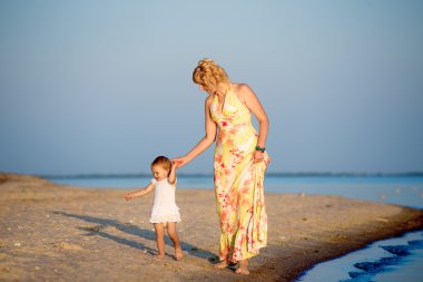 Kumsalda yürüyen küçük bir çocuk ile anne