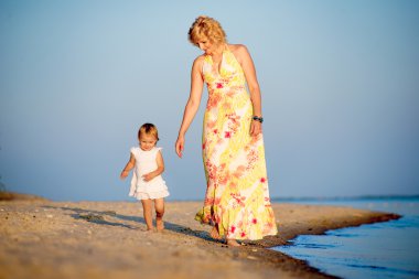 Kumsalda yürüyen küçük bir çocuk ile anne