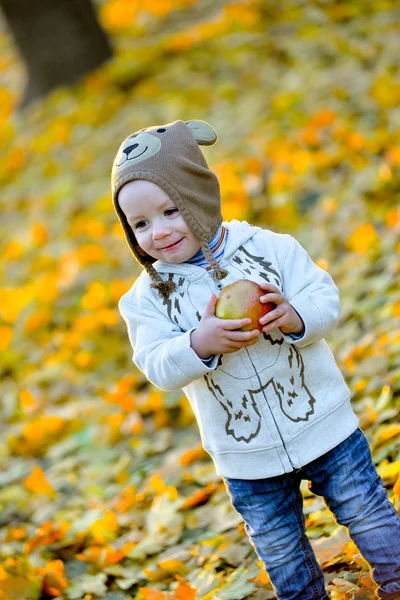 Cheerful kid with an apple in the fall — Stock Photo, Image