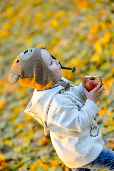 Cheerful kid with an apple in the fall — Stock Photo, Image