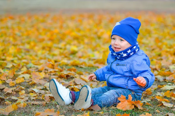 Kid sitting in the yellow leaves in the park — Stock Photo, Image