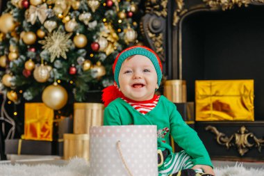 Elf gibi giyinmiş şirin bir çocuk Noel hediyesini süslü bir Noel evinde açıyor..