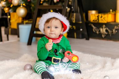 Elf gibi giyinmiş şirin bir çocuk Noel hediyesini süslü bir Noel evinde açıyor..