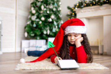 Noel Baba şapkalı küçük bir kız Noel arifesinde Noel Baba için bir mektup yazıyor..