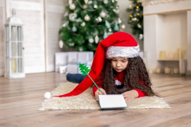 Noel Baba şapkalı küçük bir kız Noel arifesinde Noel Baba için bir mektup yazıyor..