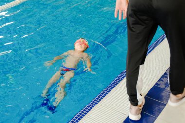 Yeni yürümeye başlayan çocuk havuzda yüzme eğitimi alıyor. Bir çocuk için yüzme eğitimi. Çocuk sporlarının gelişimi. Bebeğin sağlığını güçlendiriyor.
