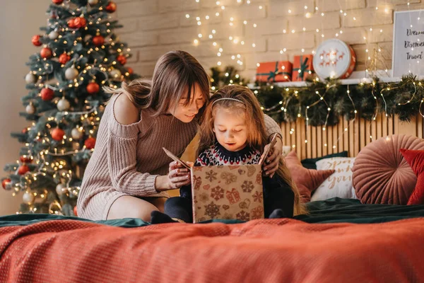 Chica emocionada con madre abre caja de regalo de Santa Claus, infancia feliz, celebración de vacaciones, milagro de Navidad —  Fotos de Stock