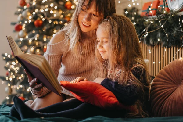 Mother and daughter reading fairytales during Christmas eve, wonderful atmosphere of love and trust, belief in miracles, happy holidays