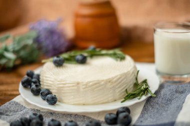 Tahta bir masada bir bardak keçi sütü ve keçi sütü peyniri standı. Peynir evde..