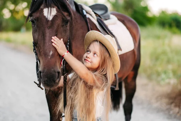 Przyjaźń dziecka z koniem. Mała dziewczynka pieszczotliwie głaszcze swojego konia. Spacerujące dziewczyny z koniem w parku jesienią. — Zdjęcie stockowe