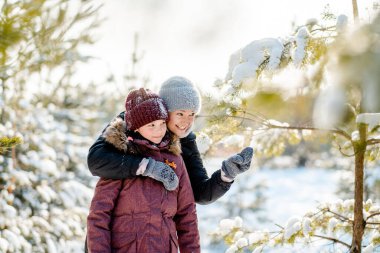 Ailece ormanda kış yürüyüşü. Çocuk büyütmek, aile alışkanlıkları. Anne ve kızı kışın güneşli ve dondurucu havada ormanda eğleniyorlar. Bir annenin kucaklaması..