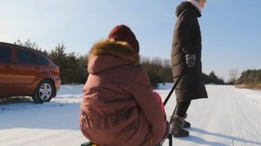 İyi tatiller. Anne ve kızının ormanda kış yürüyüşü. Anne kızını parkta karda kızağa çeker. Kış aile tatilinde parkta.