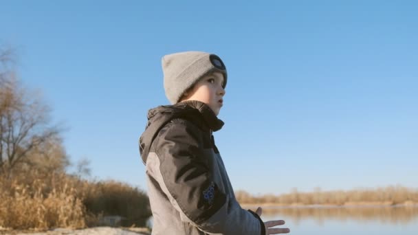 Sétálj a Michigan-tó partján. Egy fiú kora tavasszal besétál a tóhoz. Tavaszi séta egy gyerekkel a folyó közelében. — Stock videók