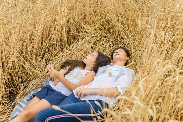 Die Mutter liegt mit ihrer Tochter im Sommer in einem Weizenfeld. Einsamkeit der Mutter mit dem Kind. — Stockfoto