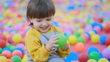 Erken çocukluk gelişimi. Bebek Geliştirme Merkezi. Neşeli küçük bir çocuk çok renkli plastik topların içinde oturuyor..