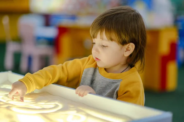 Creative child development. Baby draws sand on glass. Early development of children. Development of shallow motility and tactile sensations.