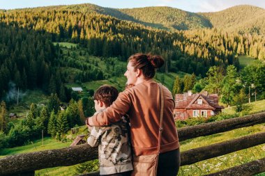 Yazın dağlarda aile tatili. Bütün aileyle birlikte dağlarda gün batımının tadını çıkarın. Çocuklarıyla birlikte bir anne bir dağ köyünde gün batımını seyrediyor..