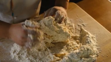 Aşçı pizza hamurunu yoğurur. Pizza pişiriyorum. Erkek bir şef pizzacının mutfağındaki ahşap masaya elleriyle hamur yoğurur..