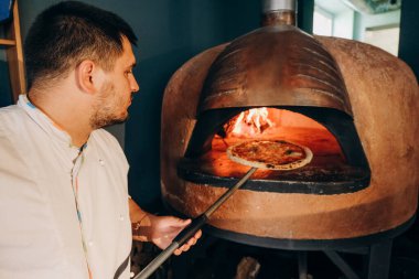 Şef ahşap fırında pizza hazırlar. Pizza pişiriyorum. Aşçı pizzayı fırına koyar..