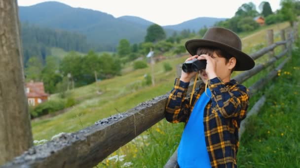 Ett barn tittar genom kikaren, stående på ett berg på sommaren. Vandring i Yellowstone National Park. Resor till Alperna med barn på sommaren. — Stockvideo