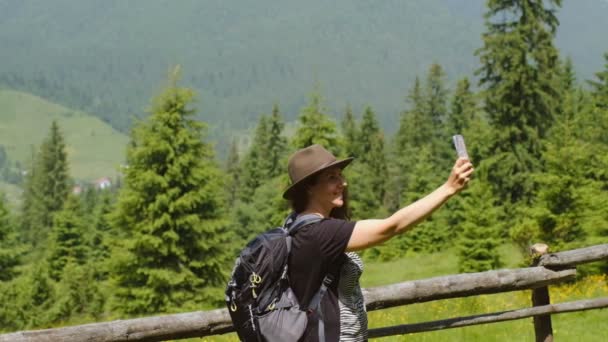 Vandring i bergen i USA. Ung kvinna turist i en vacker hatt gör en selfie i det alpina berget. — Stockvideo