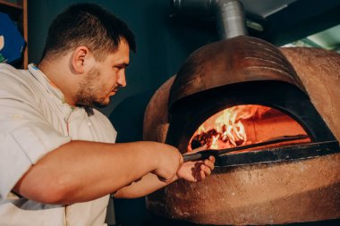 Şef ahşap fırında pizza hazırlar. Pizza pişiriyorum. Aşçı pizzayı fırına koyar. Fırından çıkan lezzetli pizza..