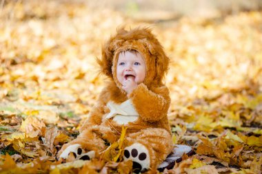 Aslan kostümlü çocuk parktaki sarı sonbahar yapraklarında oynuyor. Çocuğun neşeli ve mutlu bir çocukluğu..