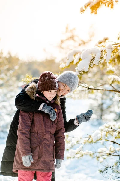 Paseo familiar de invierno en el bosque. Criar a un niño, hábitos familiares. Madre e hija se están divirtiendo en invierno en el bosque en un clima soleado y helado. Un abrazo de madres. — Foto de Stock