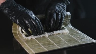 Bir Japon restoranında profesyonel suşi hazırlığı. Siyah eldivenli suşi makinesi deniz ürünleri suşisi hazırlar..