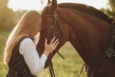 Genç ve güzel bayan jokey okşar, atların başına sarılır ve yarışmaya hazırlanır. Yaz akşamları çayırda atlama eğitimi..