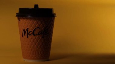 Masanın üzerinde sarı bir McCoffee bardağı duruyor. Bardağın aydınlatma düzgünce değişiyor. Düzenleyici video.
