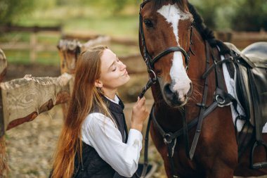 Genç bir dişi binici atının yanında duruyor ve bir yarışa hazırlanıyor. Atlama eğitimini göster. Atları severim..
